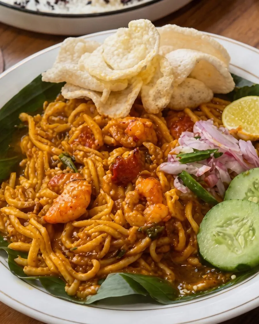 Sepiring Mie Aceh dengan udang, emping, acar bawang, timun, dan jeruk nipis di atas daun pisang